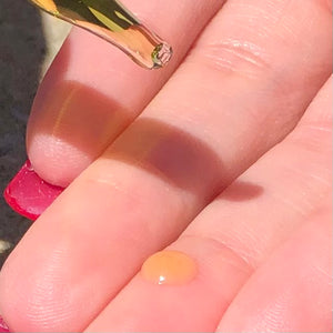 Closeup of a glass dropper and a drop of golden oil on a middle finger.